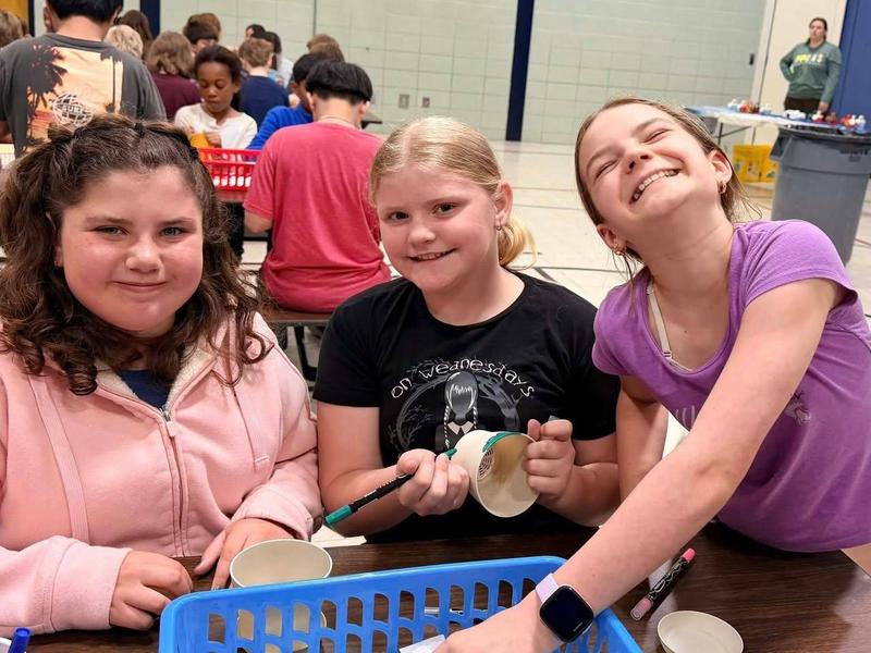 Three girls are smiling while engaging in an arts and crafts activity at a table.