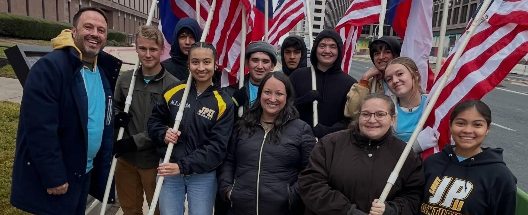 A group of young people and adults holding flags and smiling together outdoors.