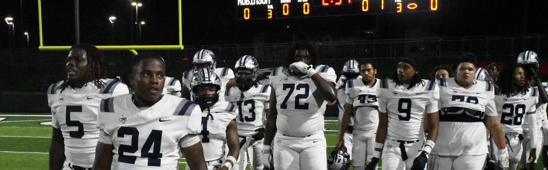 Group of football players walking together on a field at night.