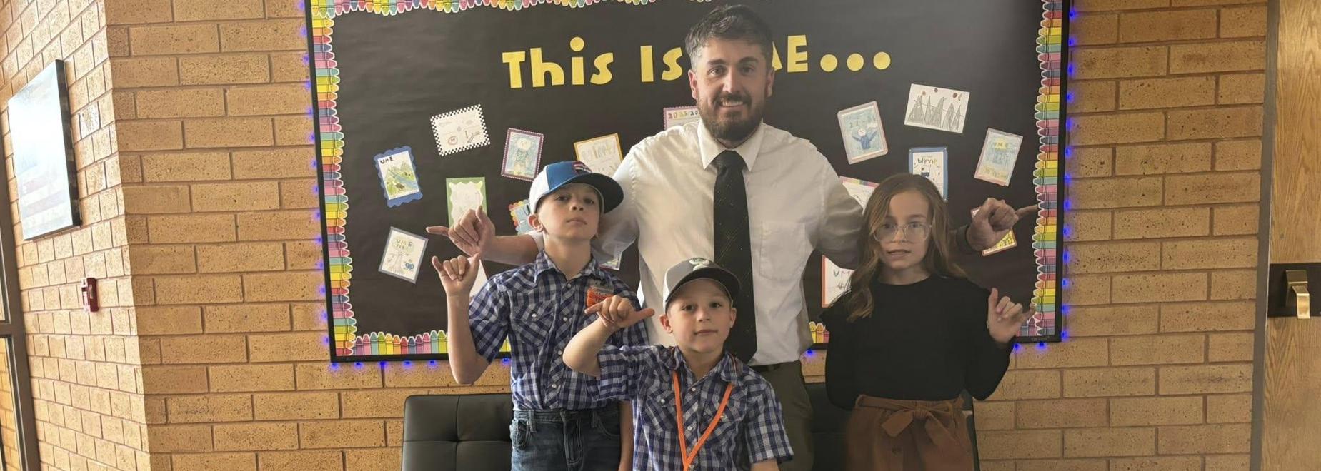 Three children posing with a man in business attire, all smiling in a school setting.