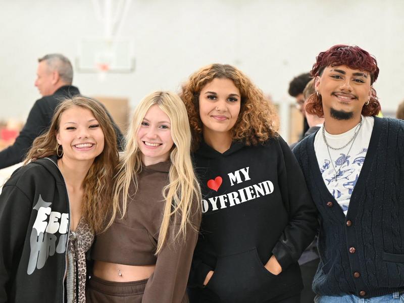 Four smiling friends posing together indoors, wearing casual outfits.
