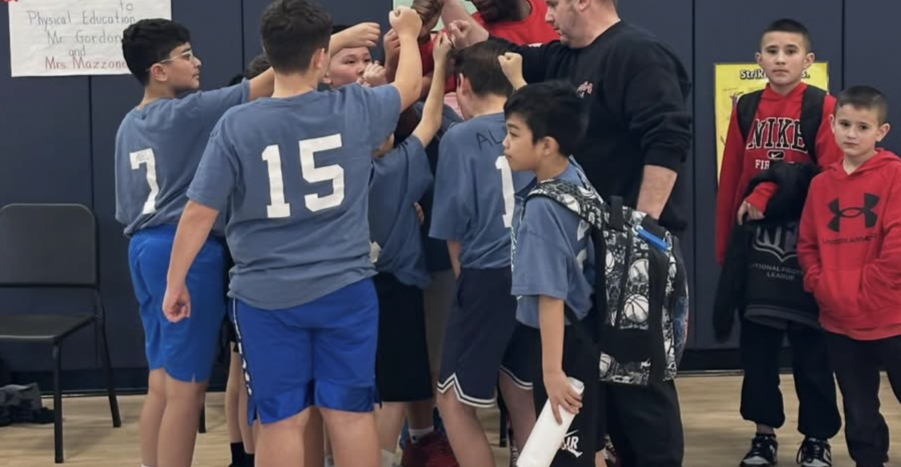 A group of boys in blue shirts huddle together during a sports activity.
