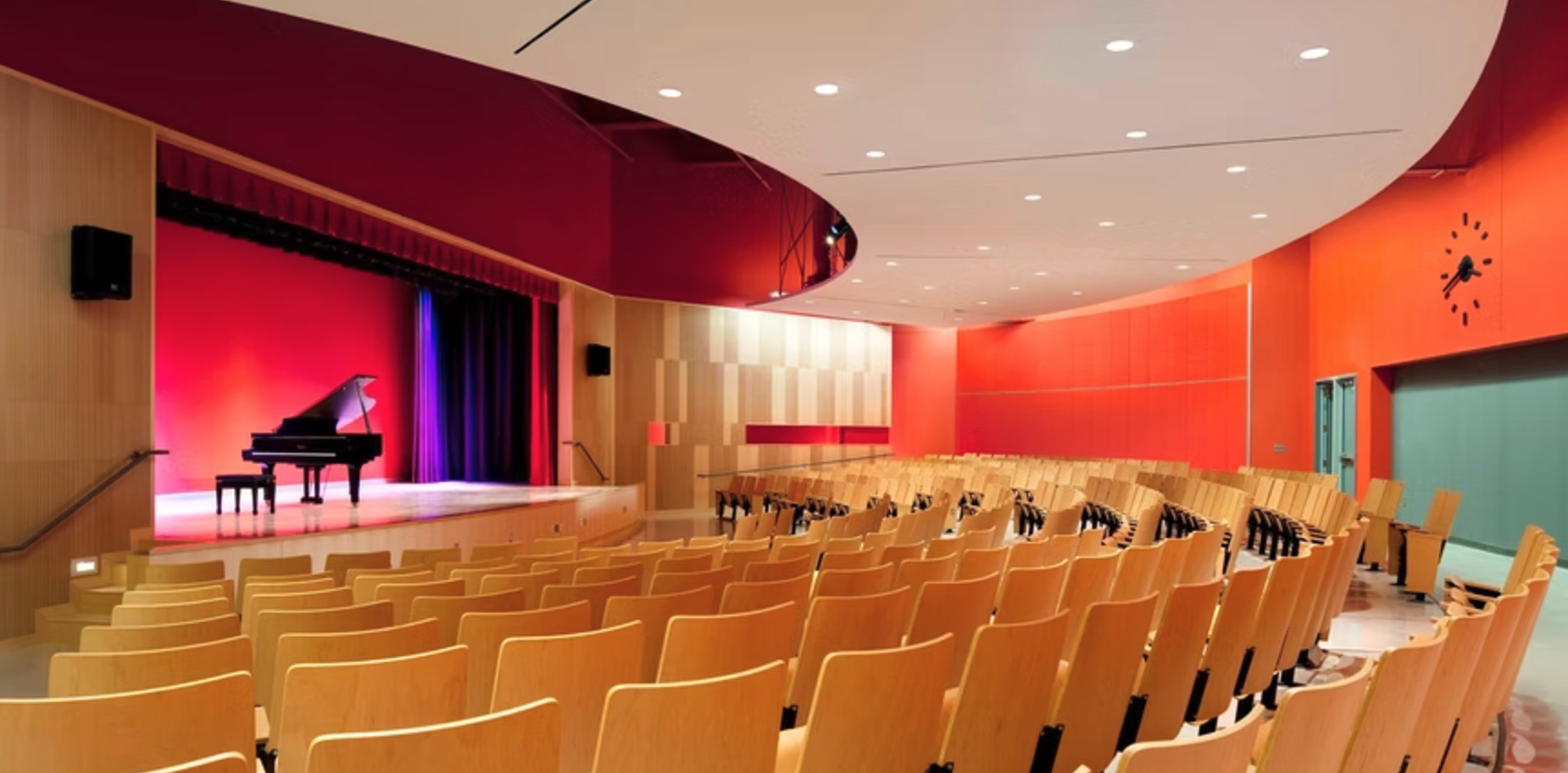 A modern auditorium with a grand piano on stage and wooden seats arranged in rows.