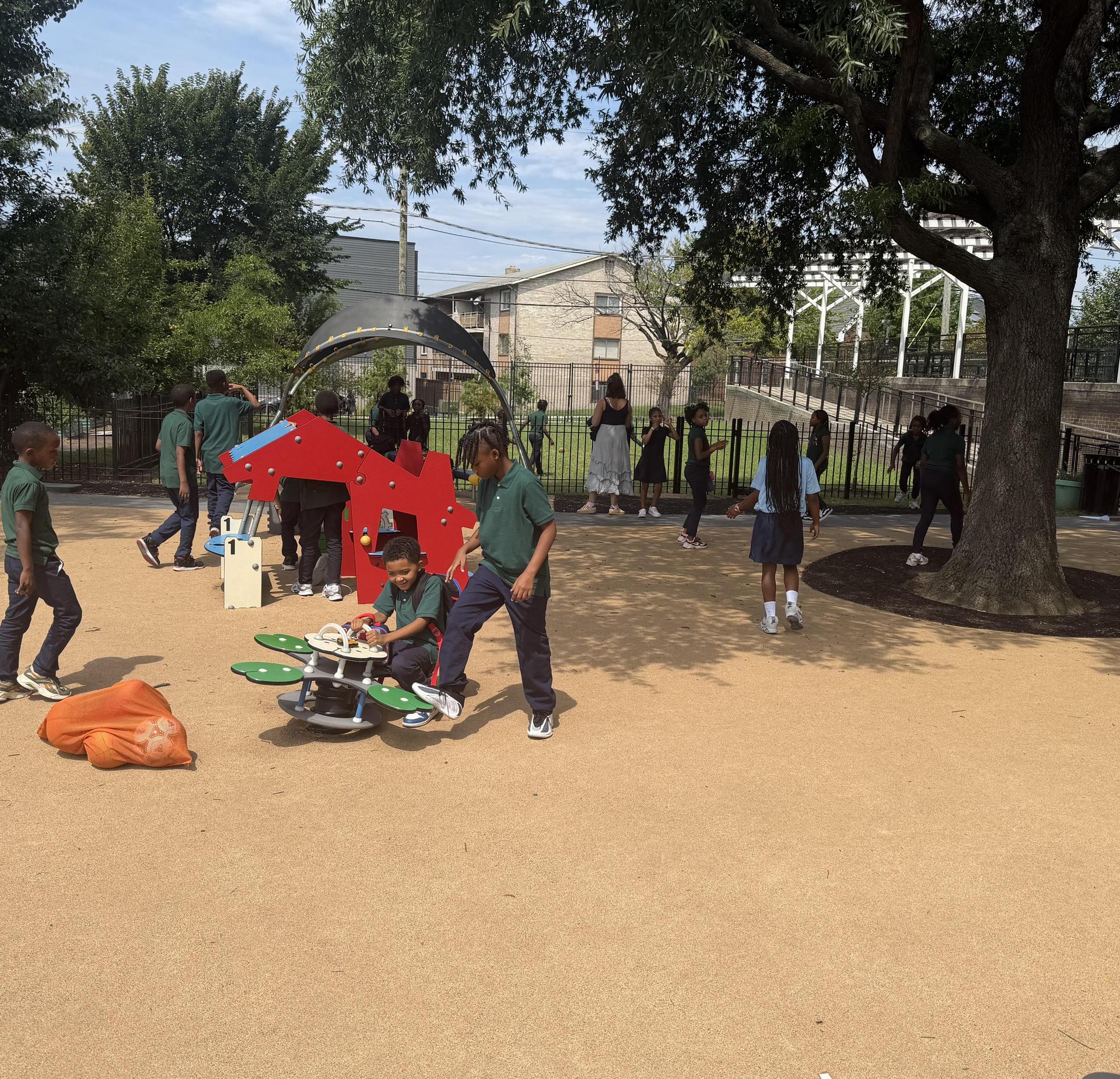 Children playing in a park with a playground and trees in the background.