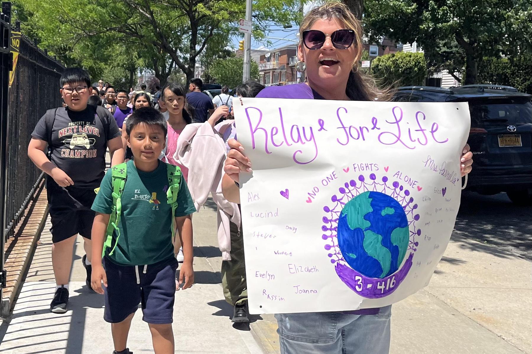 A woman and children march with a sign featuring a globe for Relay for Life.
