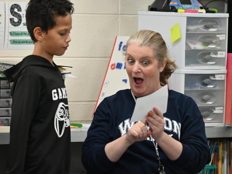 A woman showing excitement while interacting with a child in a classroom.