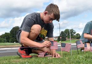 A person crouches, arranging American flags on the ground.