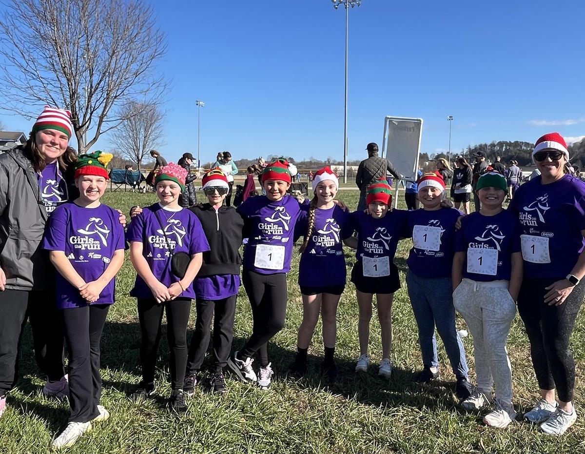 A group of girls in purple shirts with festive hats posing on a grassy field.