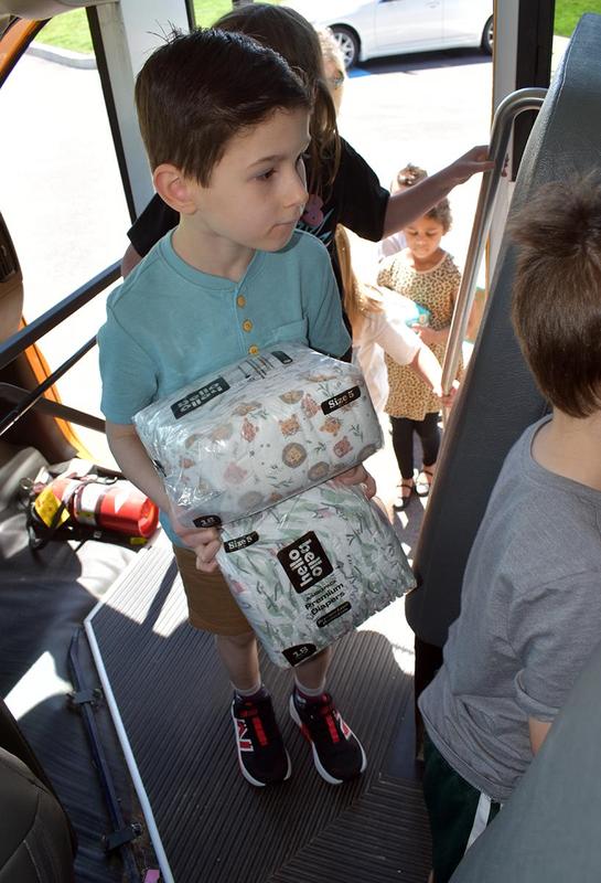 A boy holding two packs of diapers while boarding a bus.
