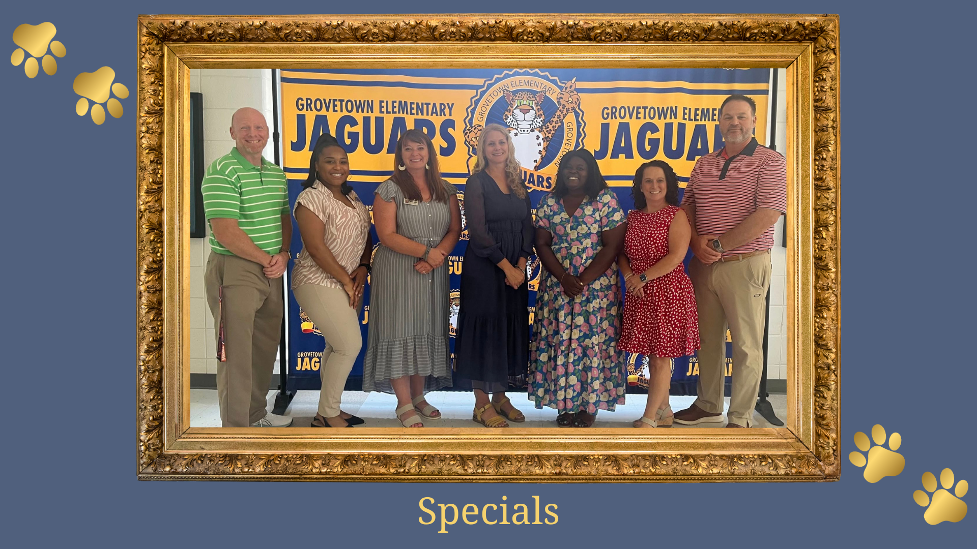 Group of staff members posing in front of a school banner.