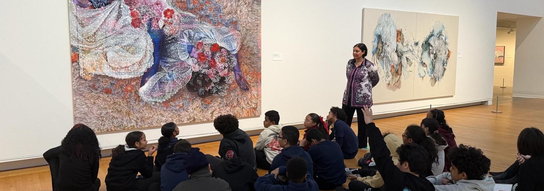 A group of students listening to a woman in front of a colorful artwork in an art gallery.
