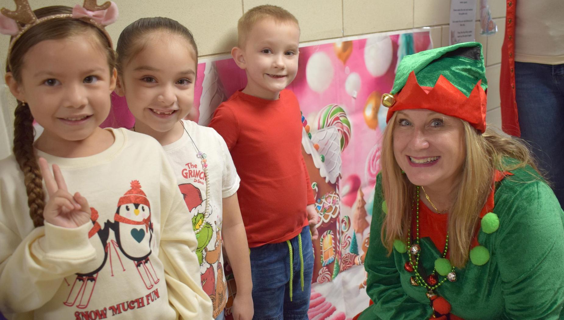 Children and an elf smiling near a colorful holiday backdrop.