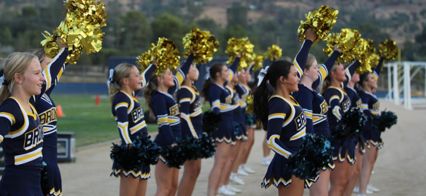 Cheerleaders in uniforms waving pom-poms on the sidelines.
