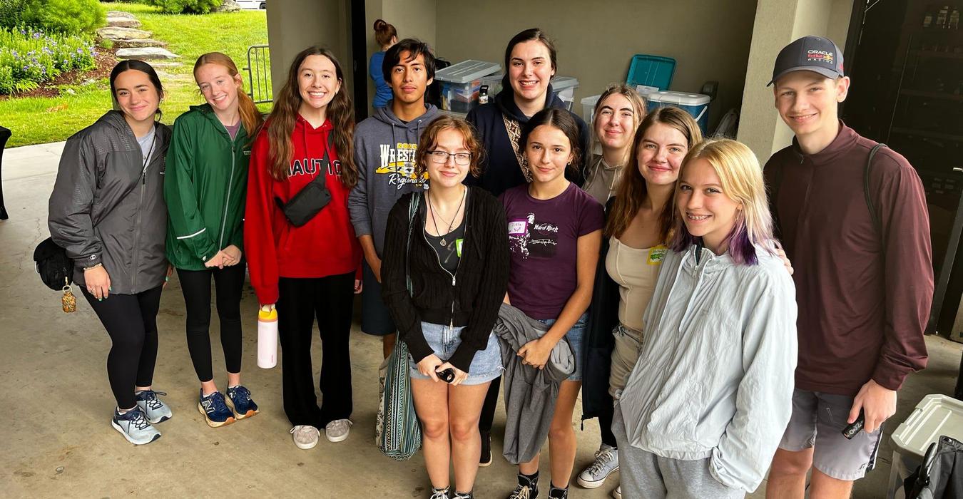 A group of young people posing together outdoors, smiling at the camera.