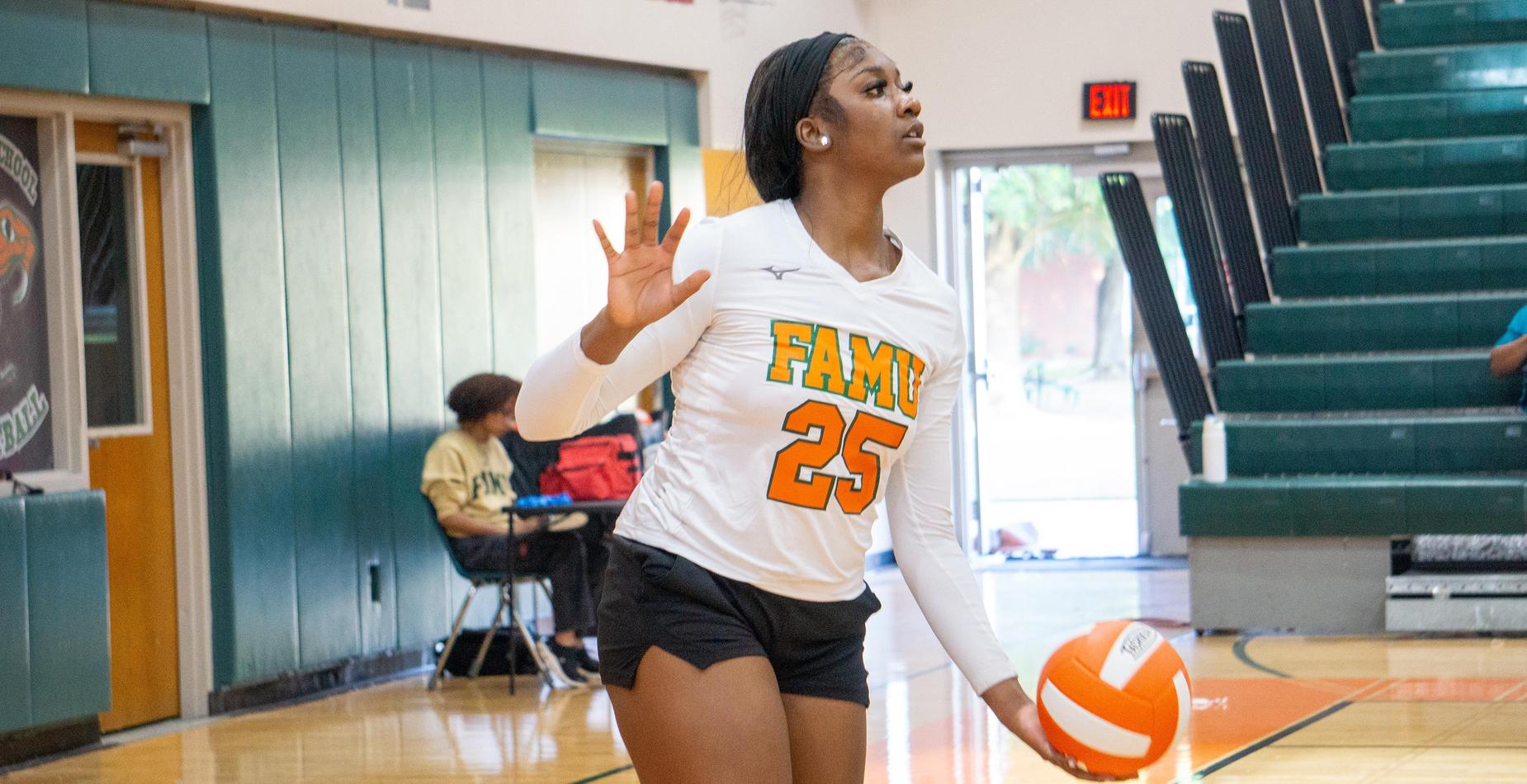 A volleyball player prepares to serve, wearing a white jersey and black shorts.