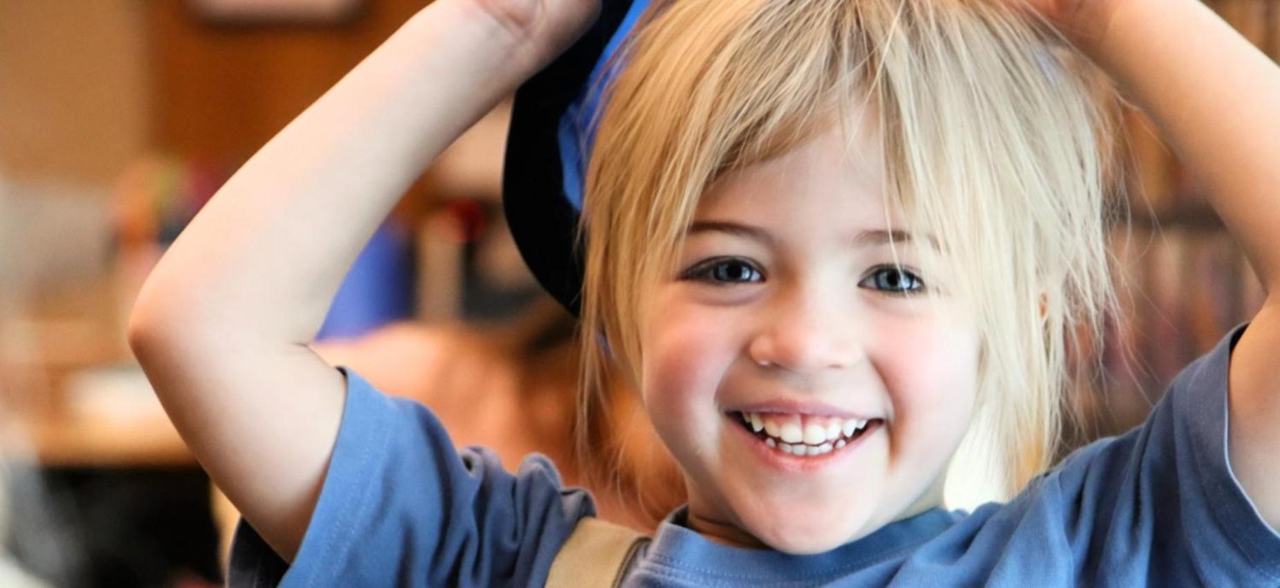 Smiling girl wearing a blue shirt and holding a hat in a cheerful setting.