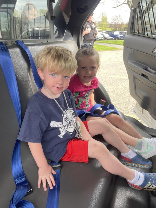 two preschoolers sit in the back of a police car