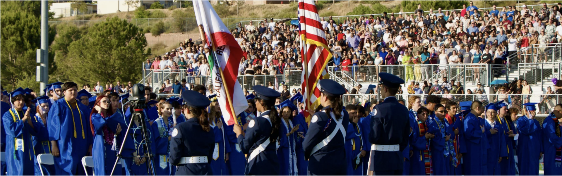 Students in military uniform holding the US flag and California flag in front of a crowd. 