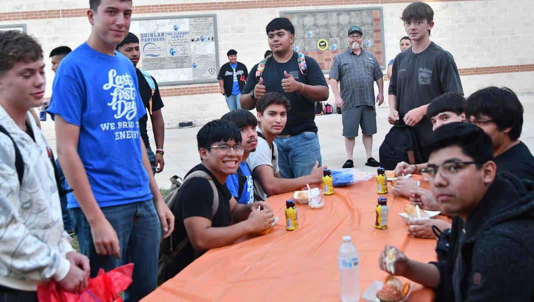 A group of young men enjoying food at a table in a school setting.