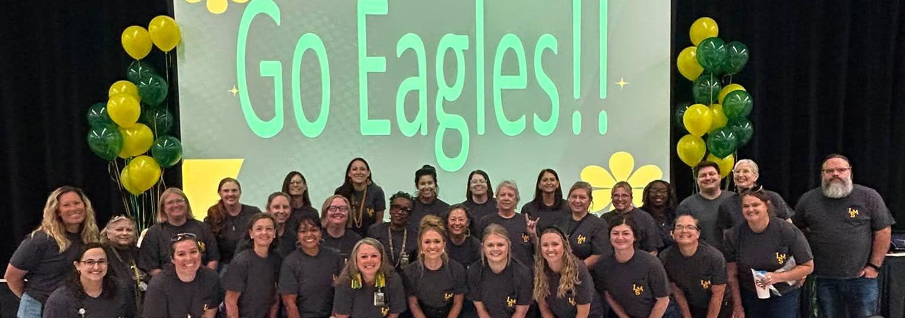 Large group of adults in matching shirts, gathered for a photo in front of a presentation screen.