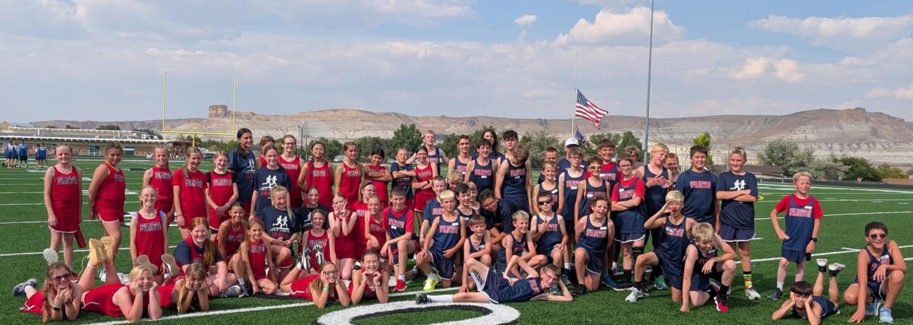 A large group of young athletes poses on a sports field with mountains in the background.