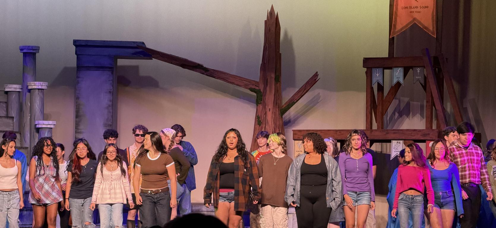 A group of performers on stage, dressed in casual outfits, singing together.