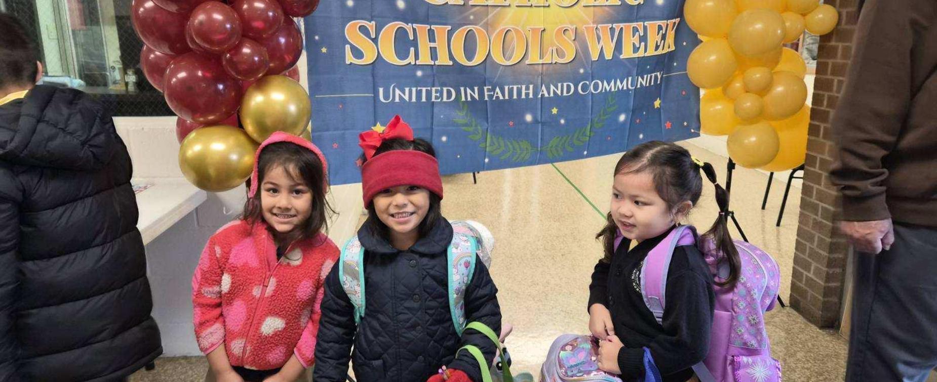 Three girls smiling at a back-to-school celebration under a colorful banner.