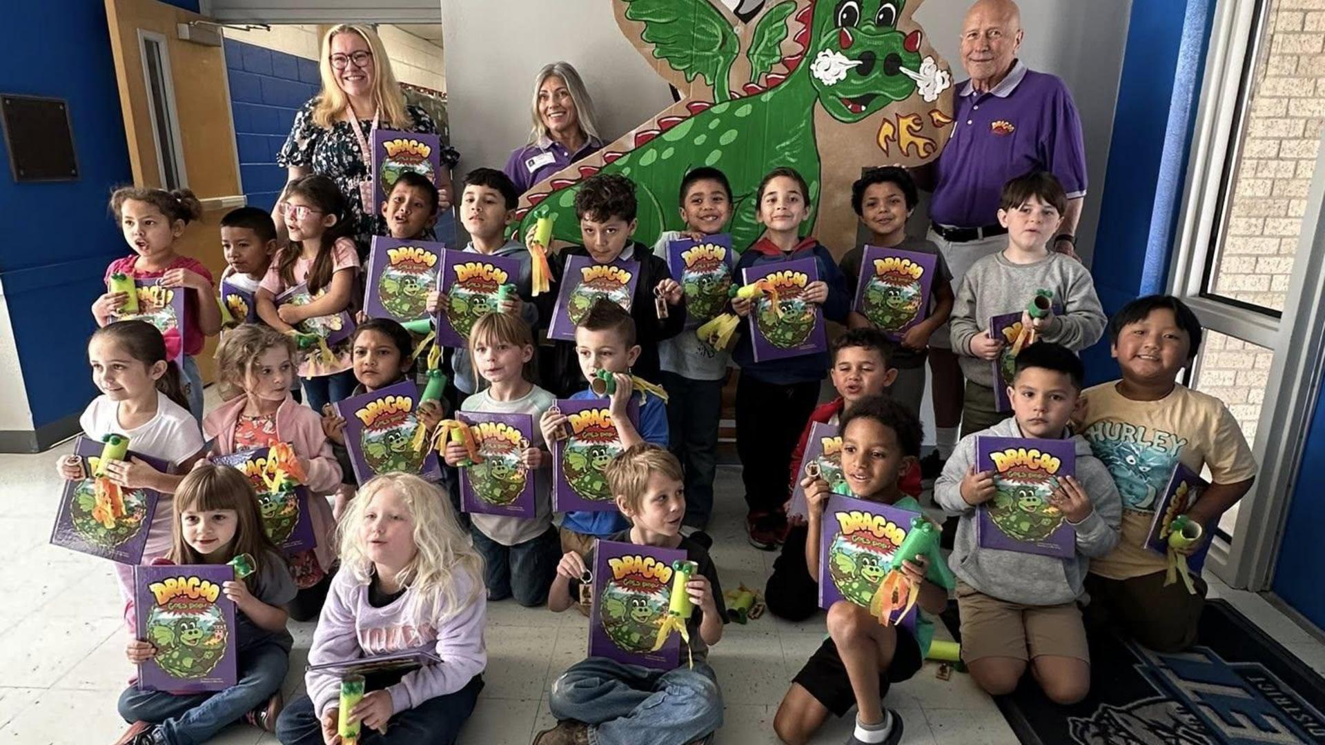 Group of children and adults posing with books and toys in a colorful setting.