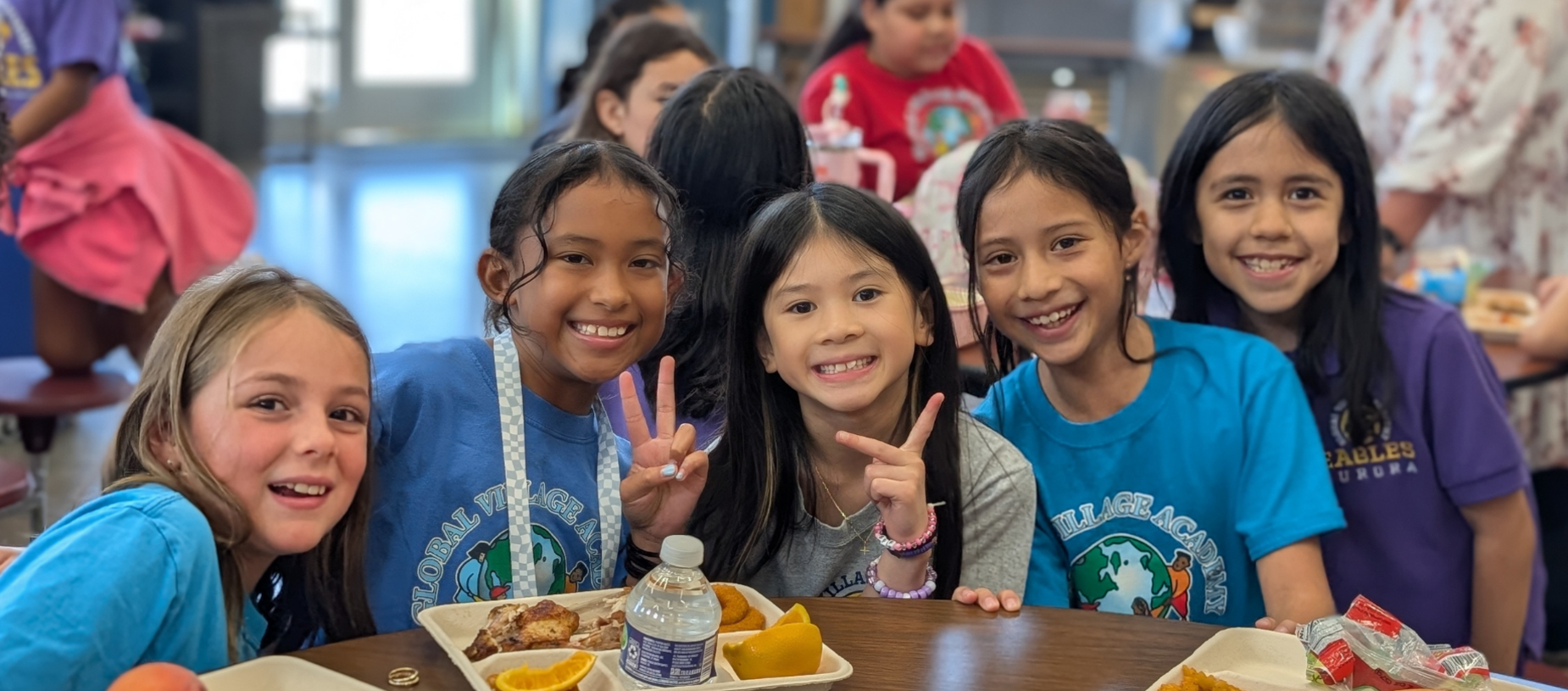 Five elementary students smiling together around a lunch table