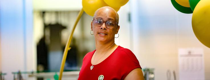 Smiling woman in a red shirt with glasses, surrounded by yellow balloons.