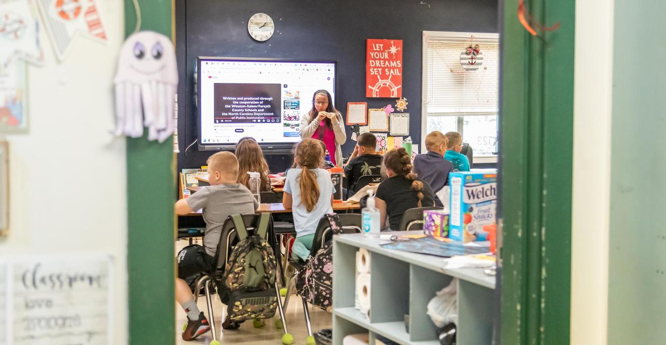 Students in a classroom engaged in a lesson with a teacher at the front.