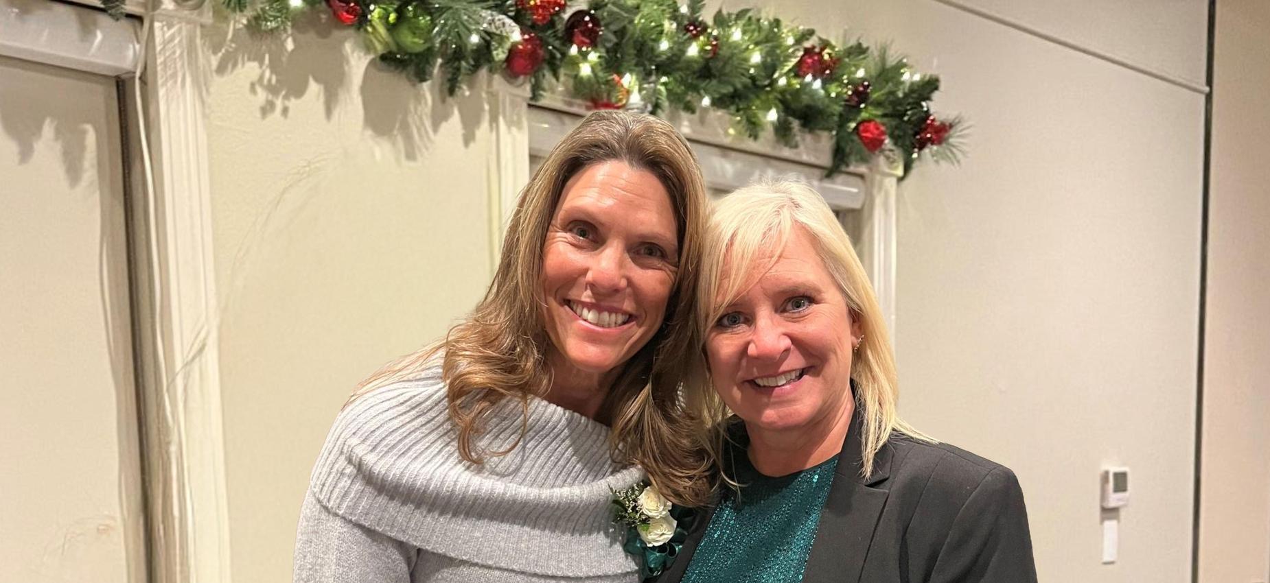 Two women smiling together at a formal event, one wearing a sweater and the other a blazer.