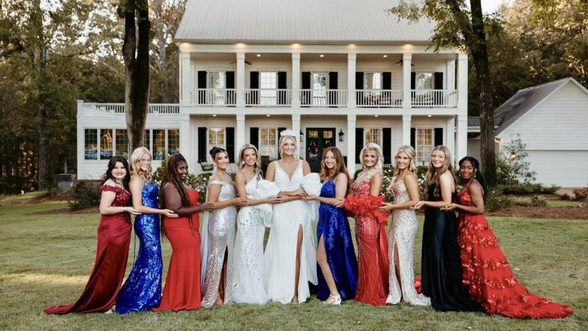 Bridesmaids in colorful dresses pose in front of a large house.