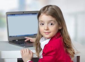 Smiling girl in a red jacket sitting at a table with a laptop.