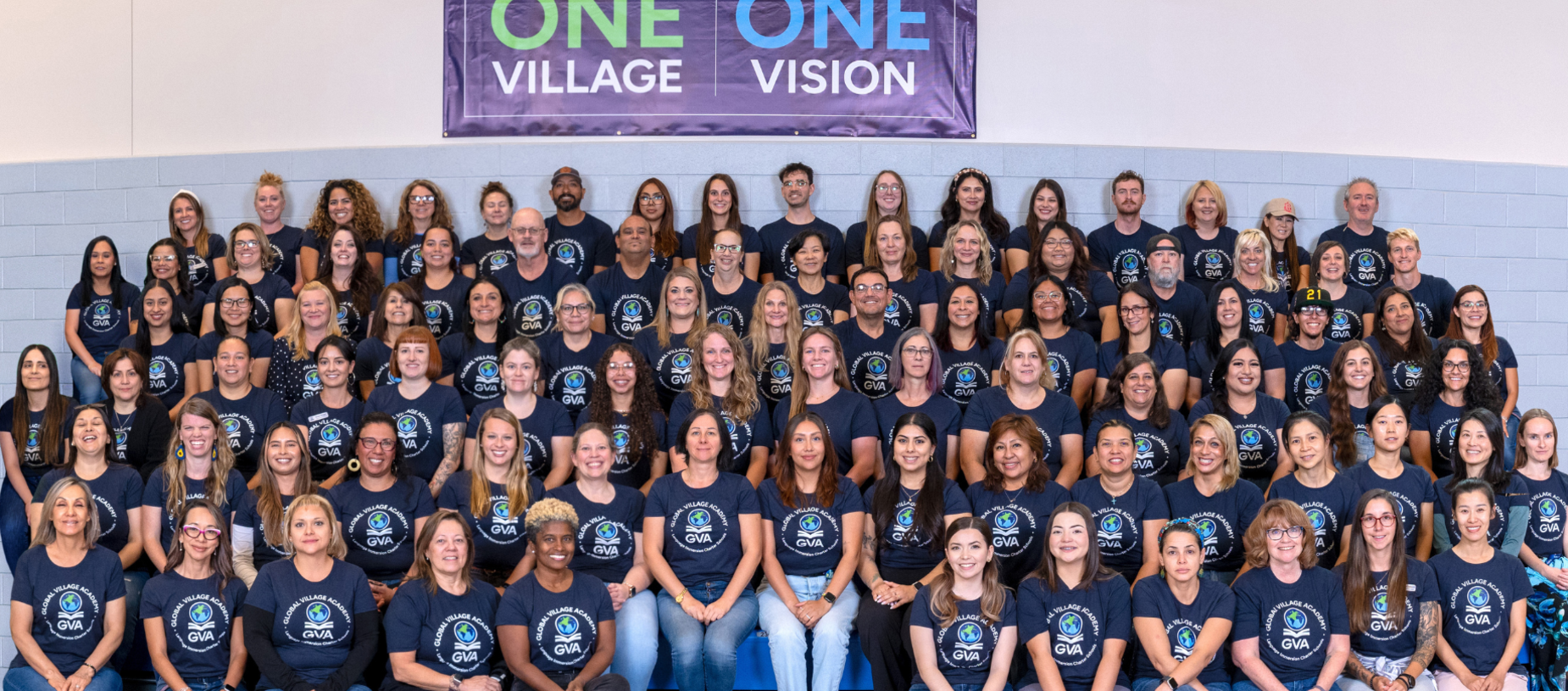 Group photo of diverse individuals wearing matching t-shirts in a gymnasium setting.