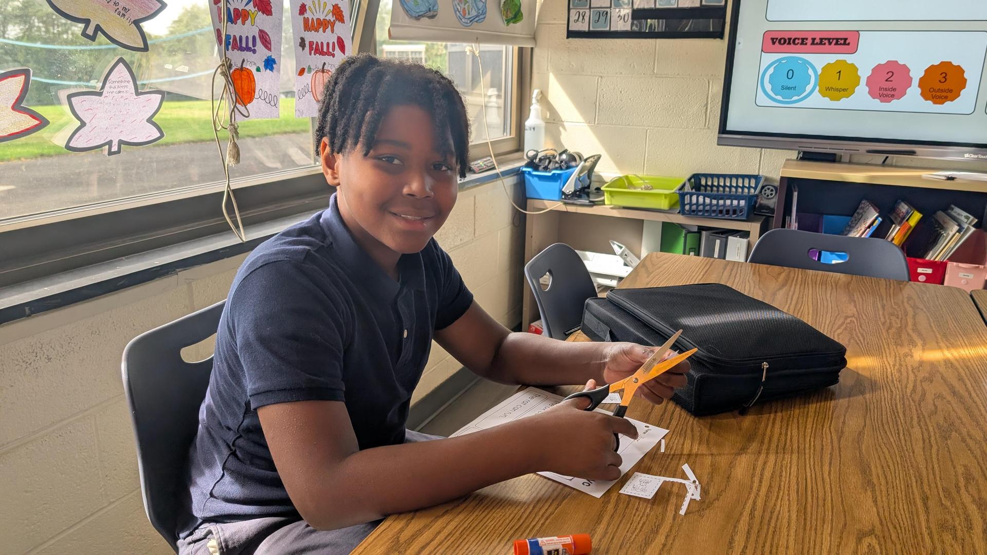 Student preparing his work for a class project using scissor at the table. 