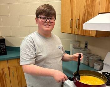 TSB student practices independent living skills while cooking at a stove.