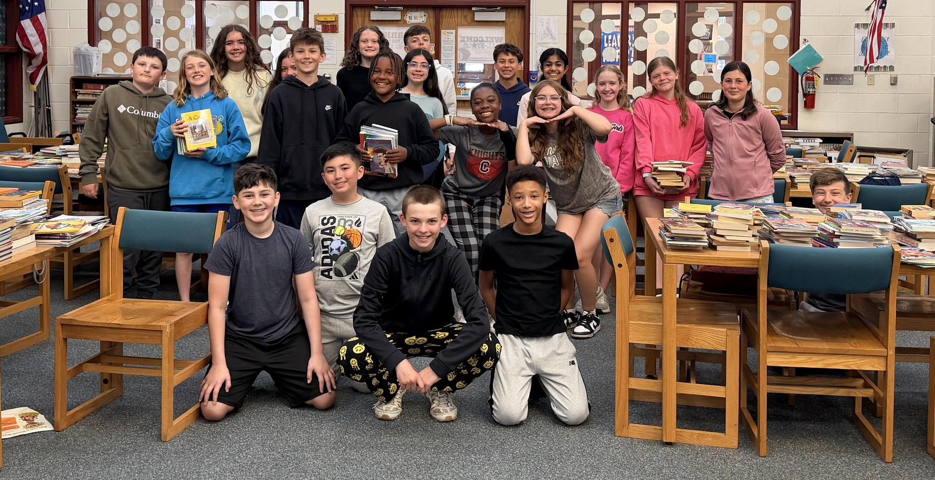 Group photo of the Hilda Walker students who sorted and boxed books that were donated in a book drive for Bernie&rsquo;s Book Bank in May. The photo is taken in the school's library and the tables around the students are filled with stacks of donated books.