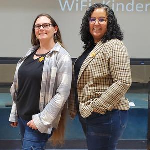 Two PUSD staff members wearing star badges pose in front of a Kinder Round-Up presentation screen.