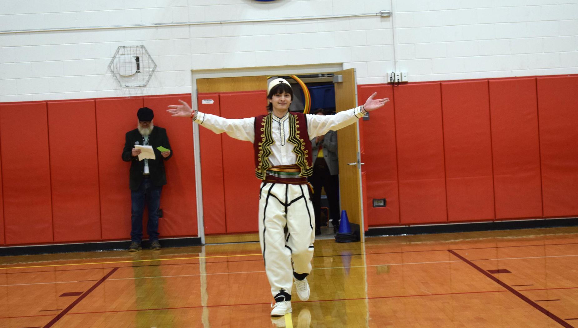 A young man in traditional attire gestures excitedly in a gymnasium.