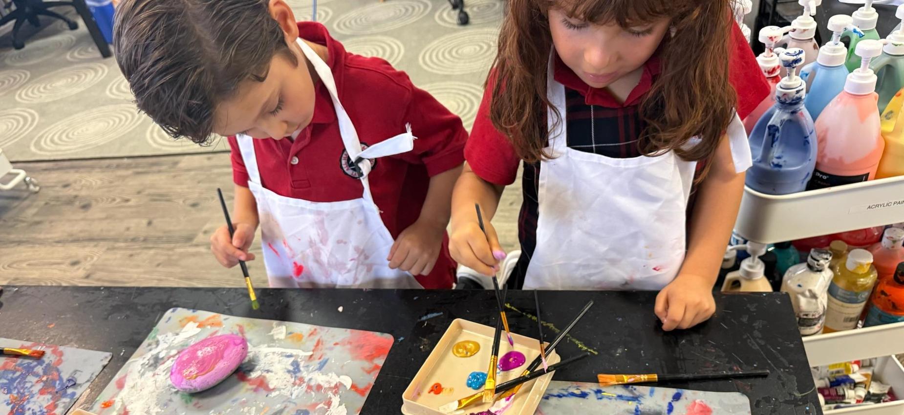 Tk students participate in art wearing paint smocks and painting with brushes