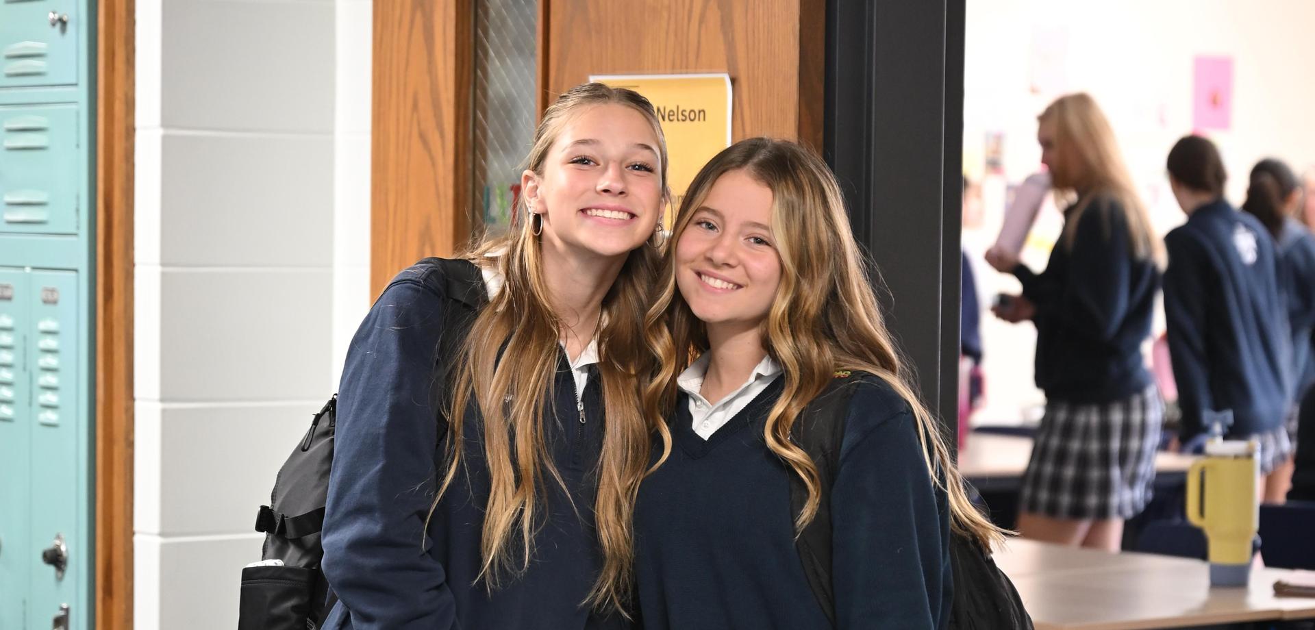 Two girls smiling together in a school hallway.