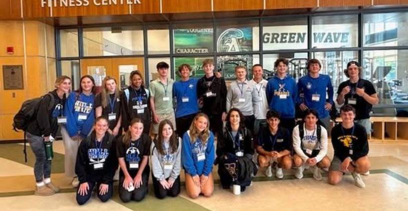 Group of students posing together at a fitness center with event badges.