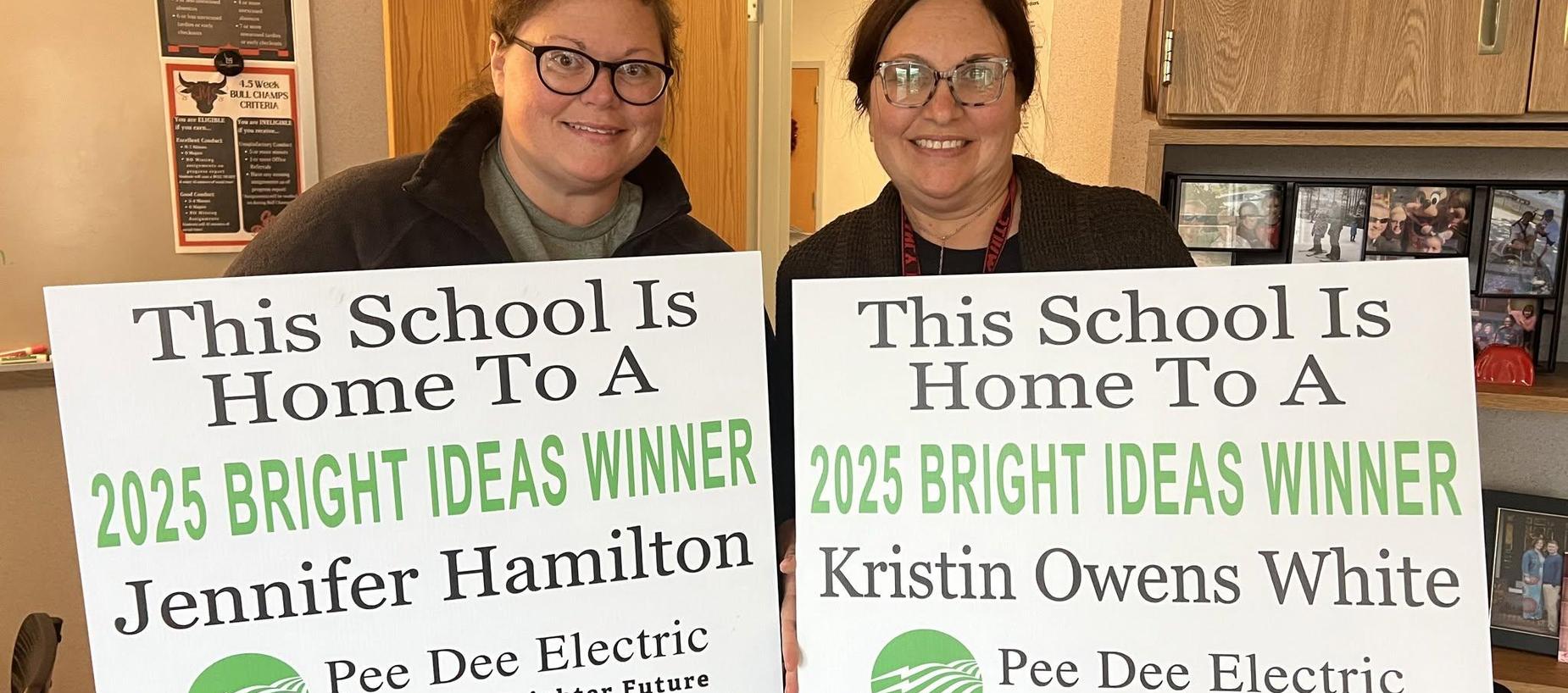 Two women holding signs announcing their Bright Ideas awards.