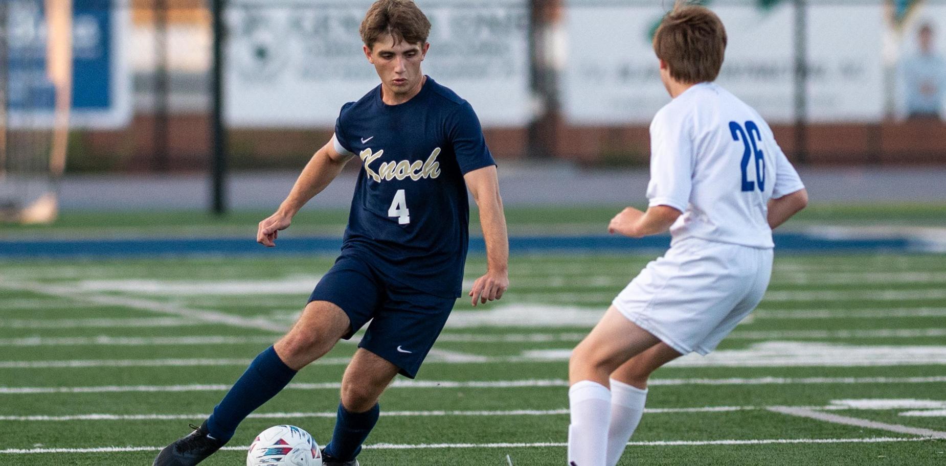 Soccer players compete on a field, focusing on a player passing the ball.