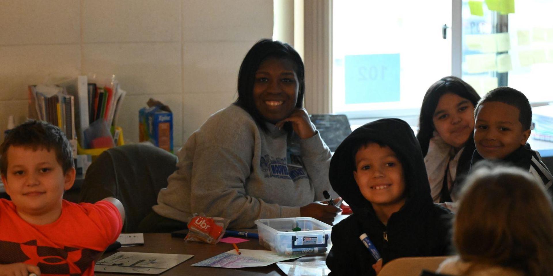 Group of children and an adult smiling while engaging at a classroom table.