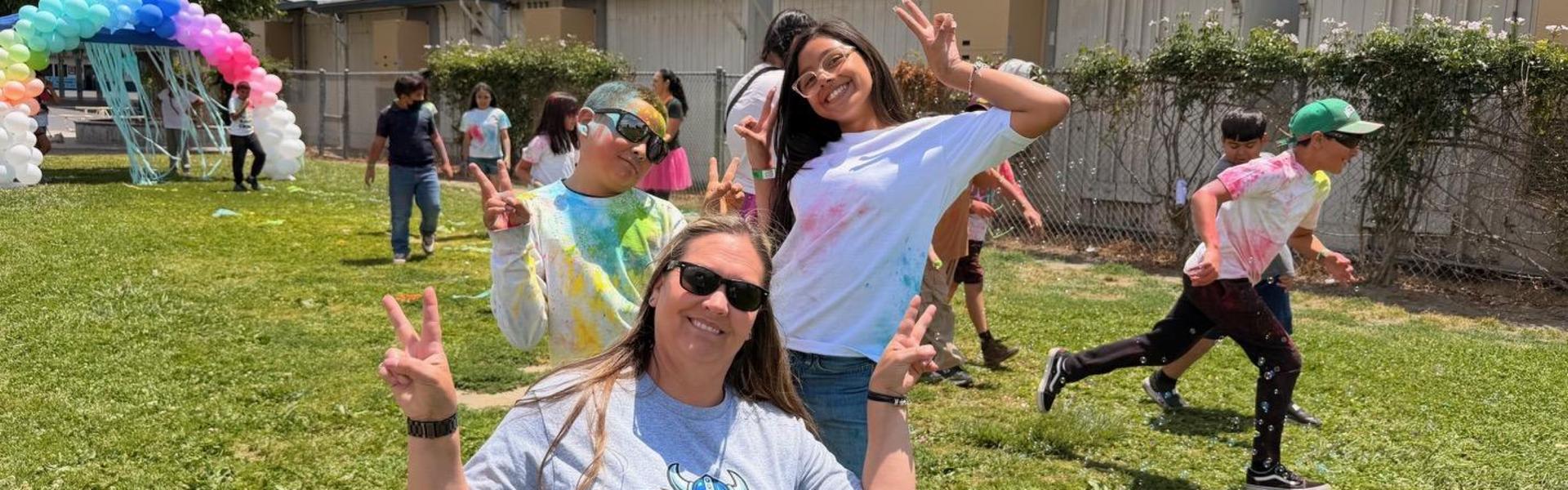 A group enjoying a colorful celebration, with a woman posing peace signs in front.