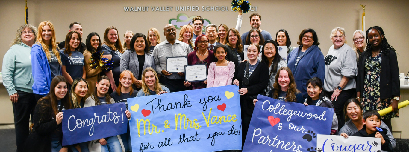 A large group of people celebrating with signs for Mr. and Mrs. Vance at a school event.