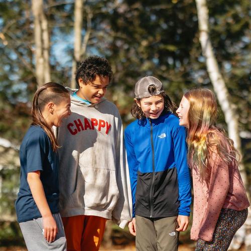 Four children laughing together outdoors in a forest setting.