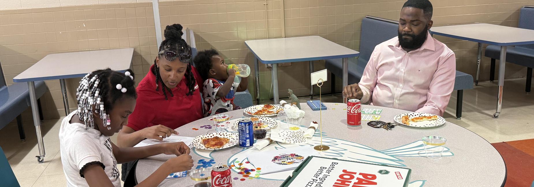 A family sitting at a table with food, drinks, and bingo cards, laughing together.